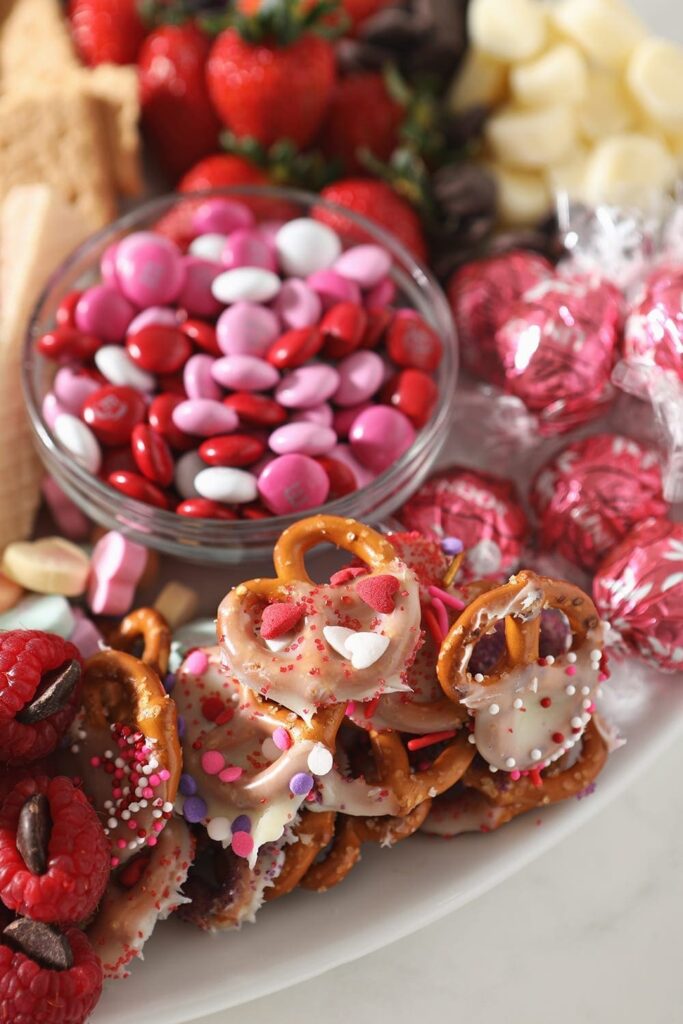 Close up of pink and white ingredients, including candies, white chocolate pretzels and more, on the platter