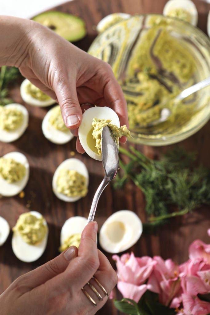 A woman scoops filling into a hardboiled egg white with a spoon, from above