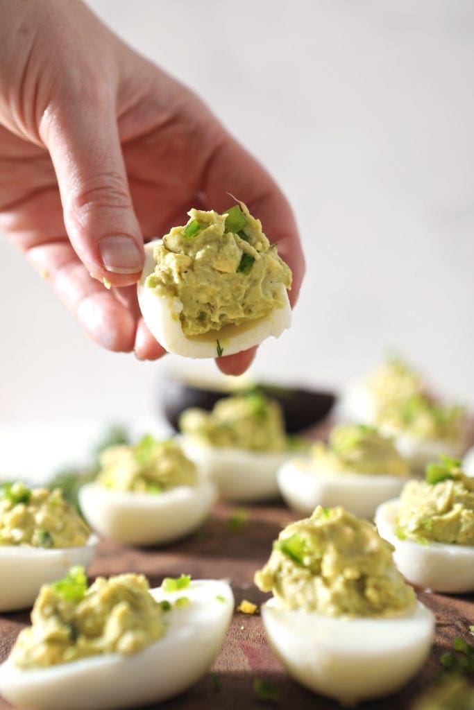 A woman holds a bitten-into Avocado Deviled Egg, from the side showing the filling