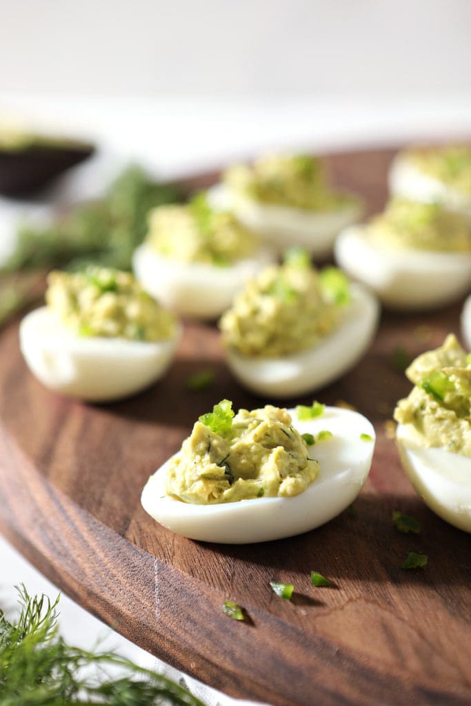 Avocado Deviled Eggs are served on a walnut board, from the side