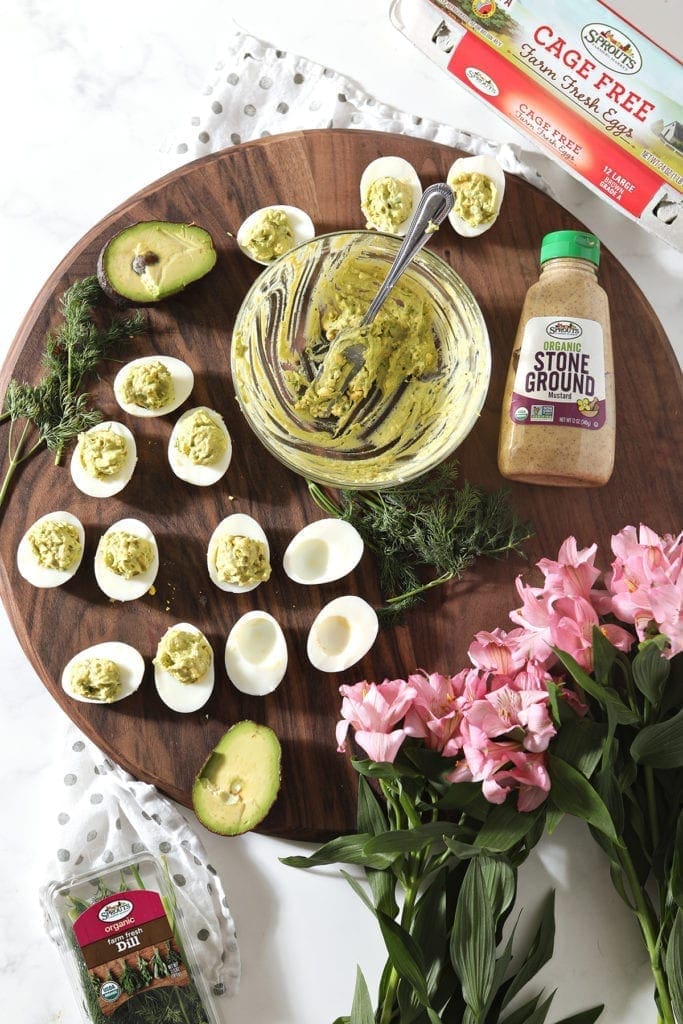 A platter of finger foods, surrounded by their ingredients and pink flowers, are shown