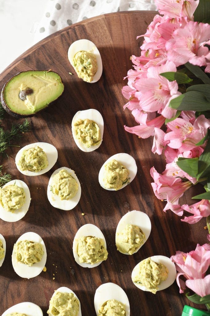 Overhead of avocado deviled eggs with pink flowers and avocados as decoration