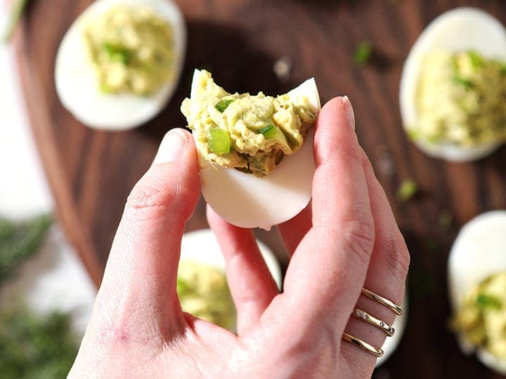 A woman holds a half-bitten deviled egg, from above