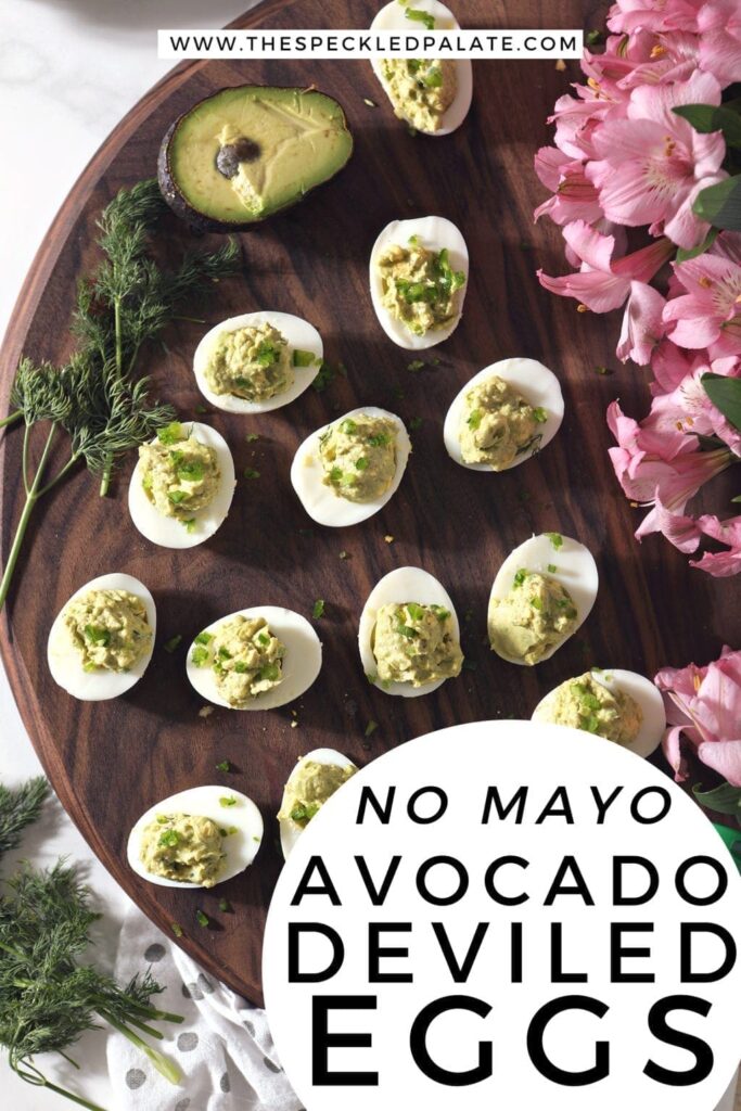 Overhead of avocado deviled eggs on a wooden board with pink flowers and Pinterest text