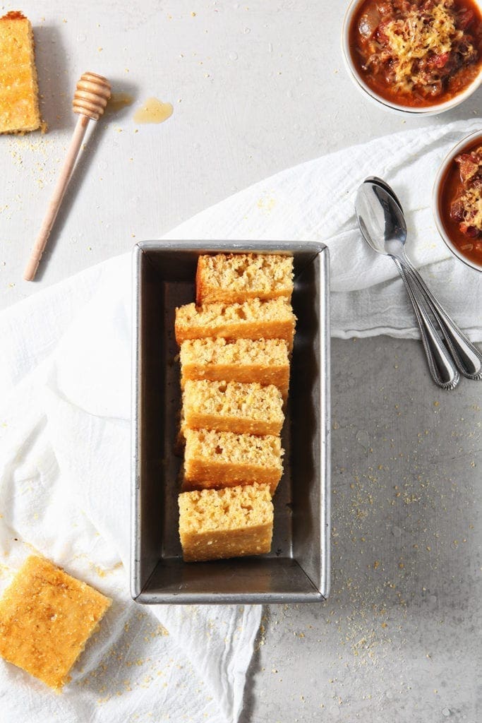 Cornbread, stacked in a baking dish, is shown with chili and ingredients from above