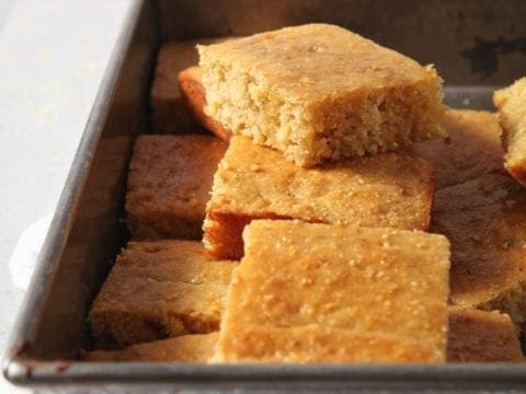 Homemade cornbread is stacked in a pan, sliced, before serving