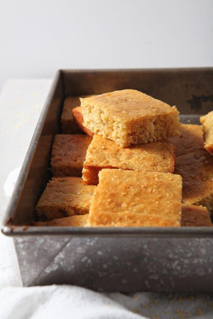 Homemade cornbread is stacked in a pan, sliced, before serving