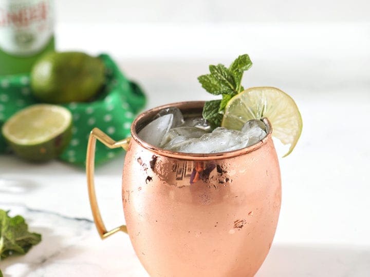A copper mug holding an Irish Whiskey Moscow Mule sits on a marble background, surrounded by ingredients