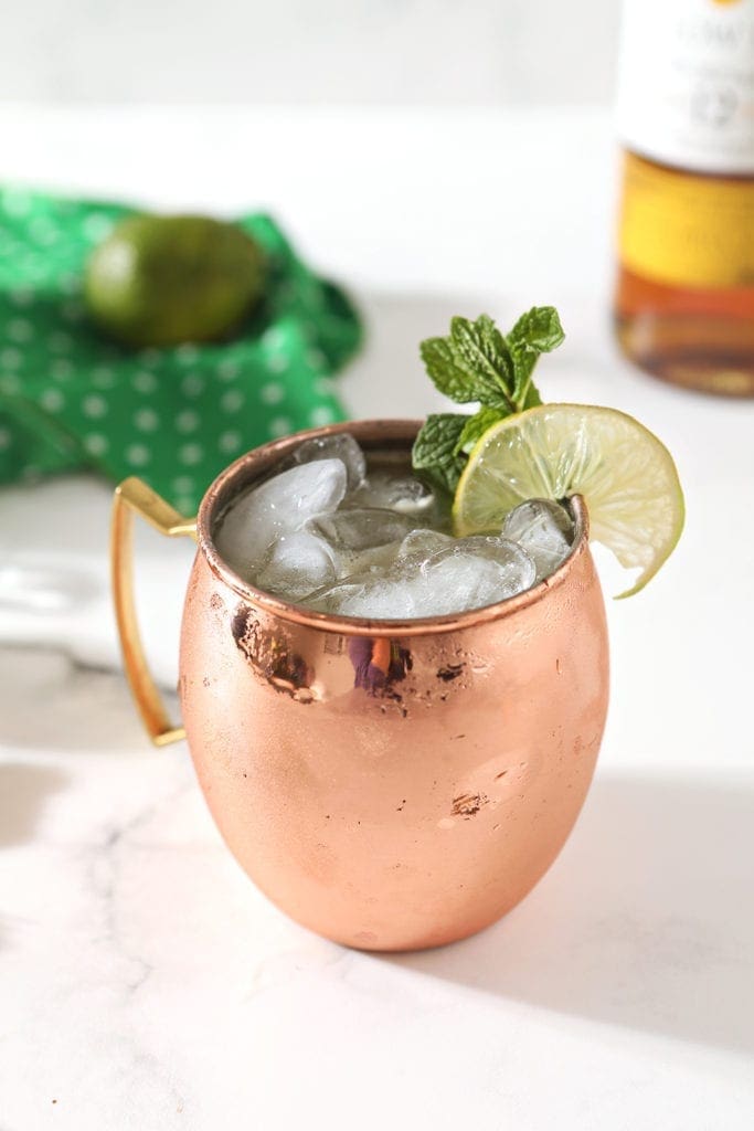 A copper mug holds an Irish Mule on a marble background, surrounded by ingredients