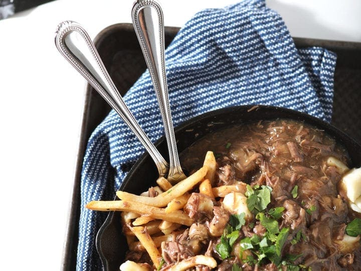 Overhead of Candian poutine in a skillet, with a meat package beside it