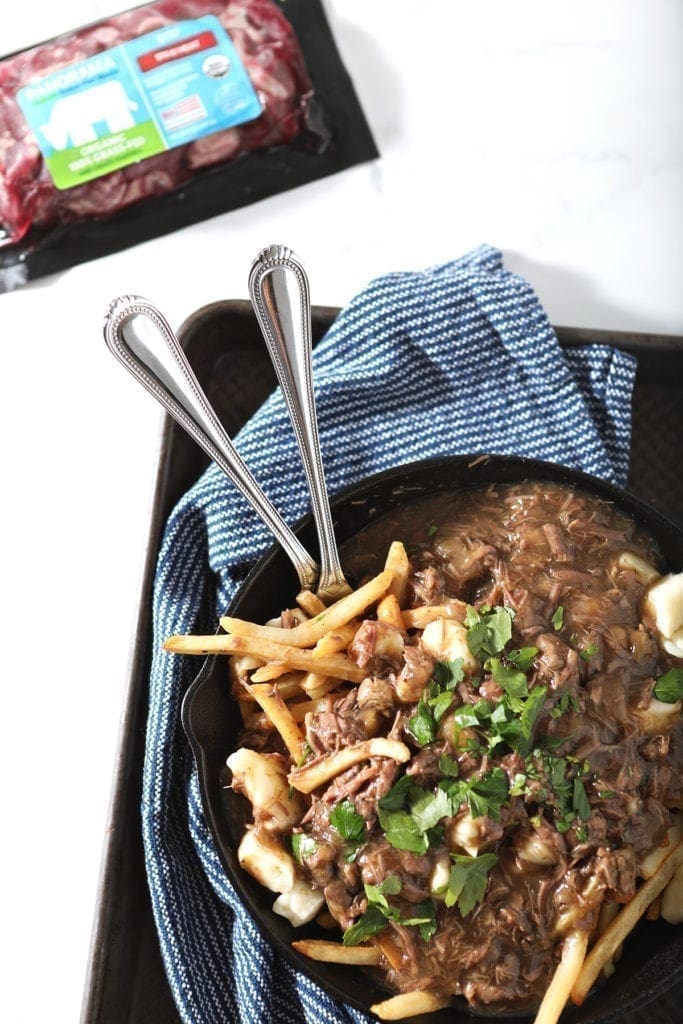 Candian poutine in a skillet with a beef stew meat package beside it