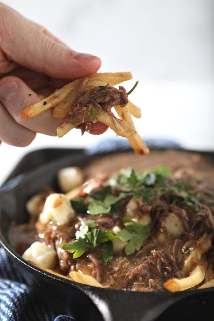 A hand holds french fries and gravy