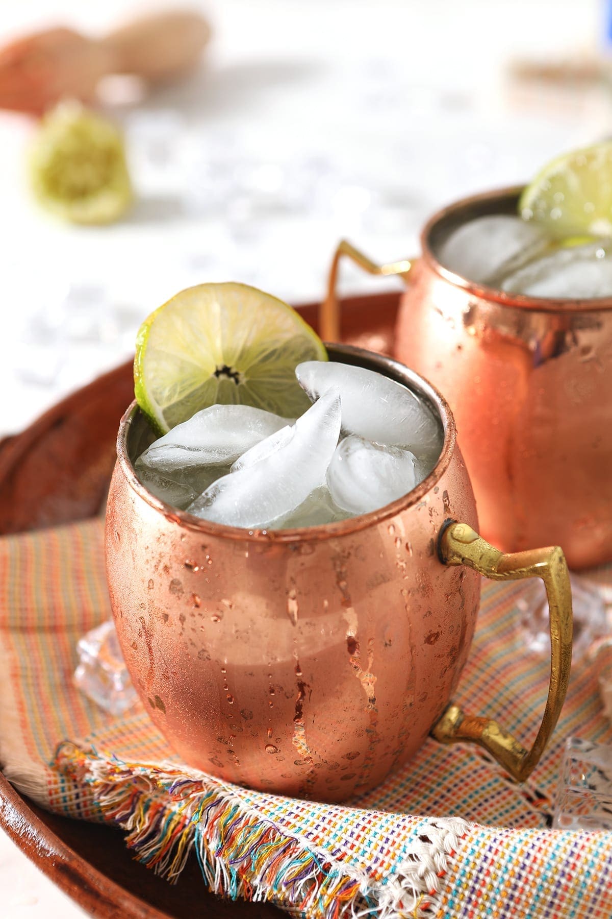 Close up of two copper mugs holding Mexican Mules, on a colorful woven platter