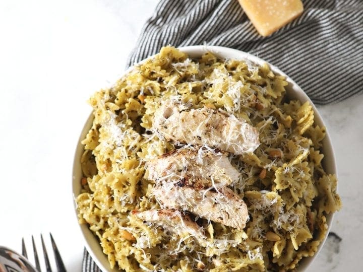 Overhead image of a white bowl holding Chicken Pesto Pasta, surrounded by ingredients