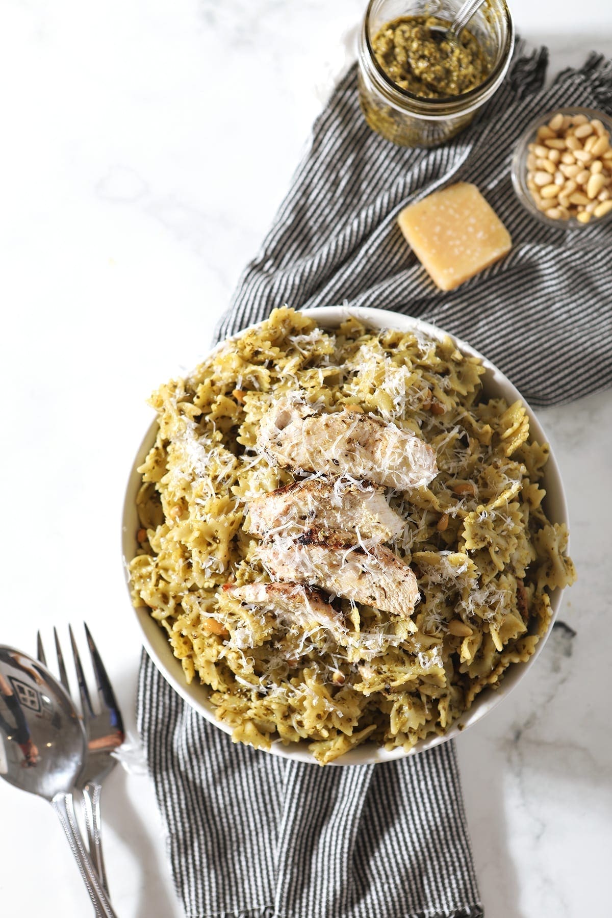 Overhead image of a white bowl holding Chicken Pesto Pasta, surrounded by ingredients