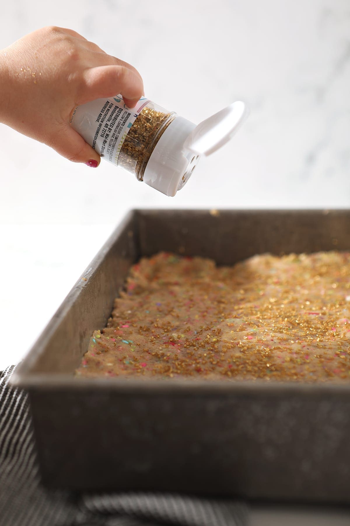 Sparkling sugar is sprinkled on top of a pan of cookie dough