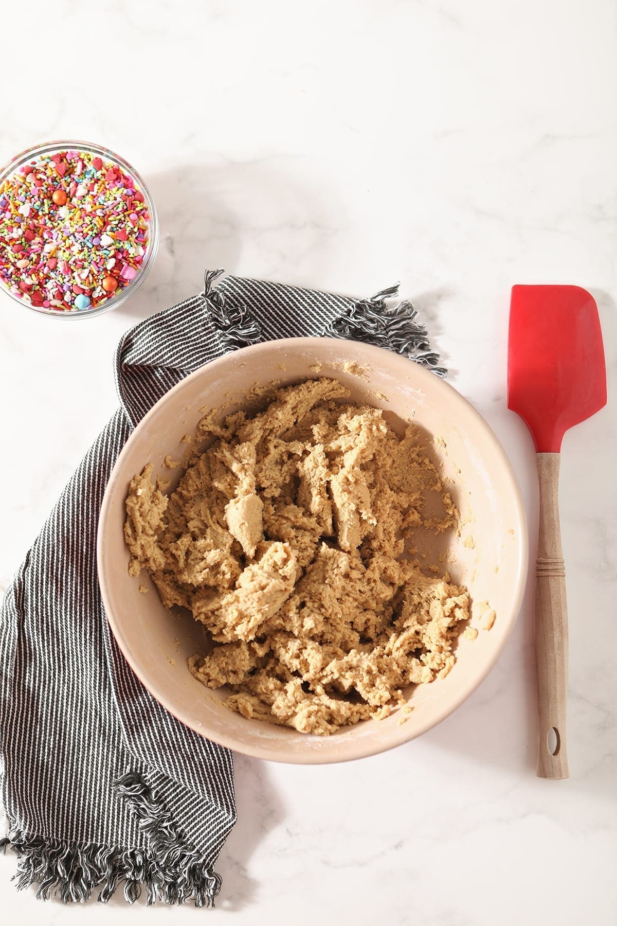 A bowl of cookie dough with a spatula and a bowl of sprinkles, from above