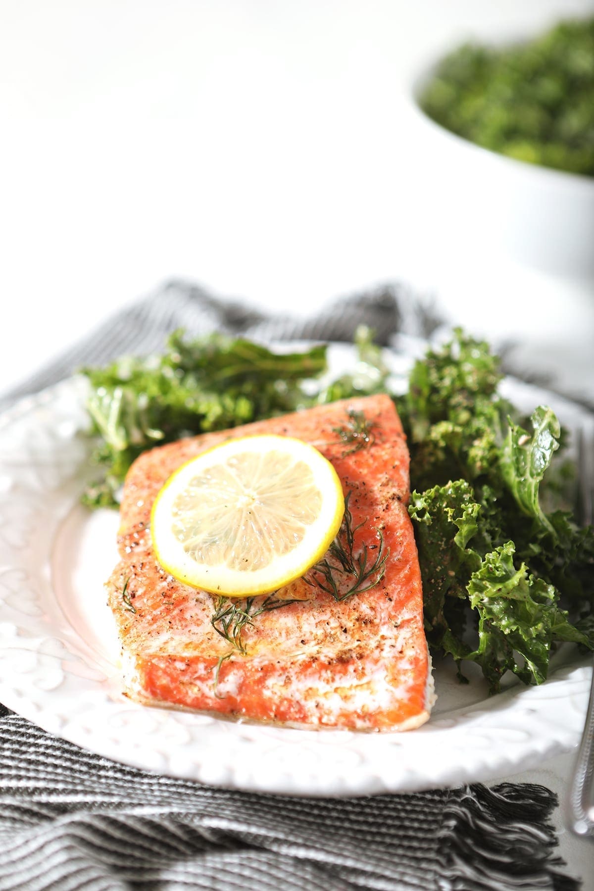 A baked salmon filet garnished with a lemon round and served with a kale salad on a white plate