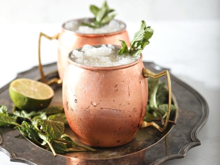 A silver platter holds two copper mugs holding Kentucky Bourbon Mules