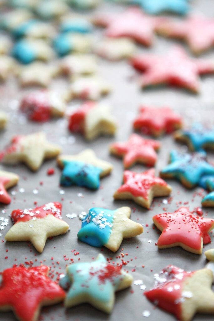 Star-shaped cookies on wax paper, after icing and sprinkles are added