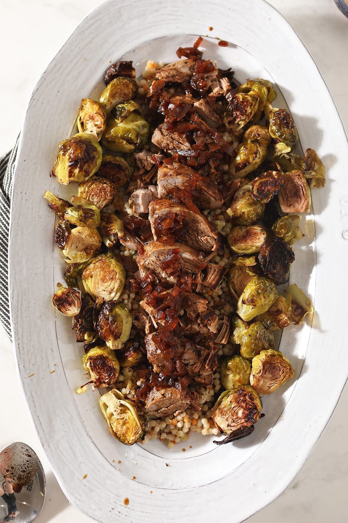 Close up of sliced pork tenderloin and brussels sprouts on a large white platter