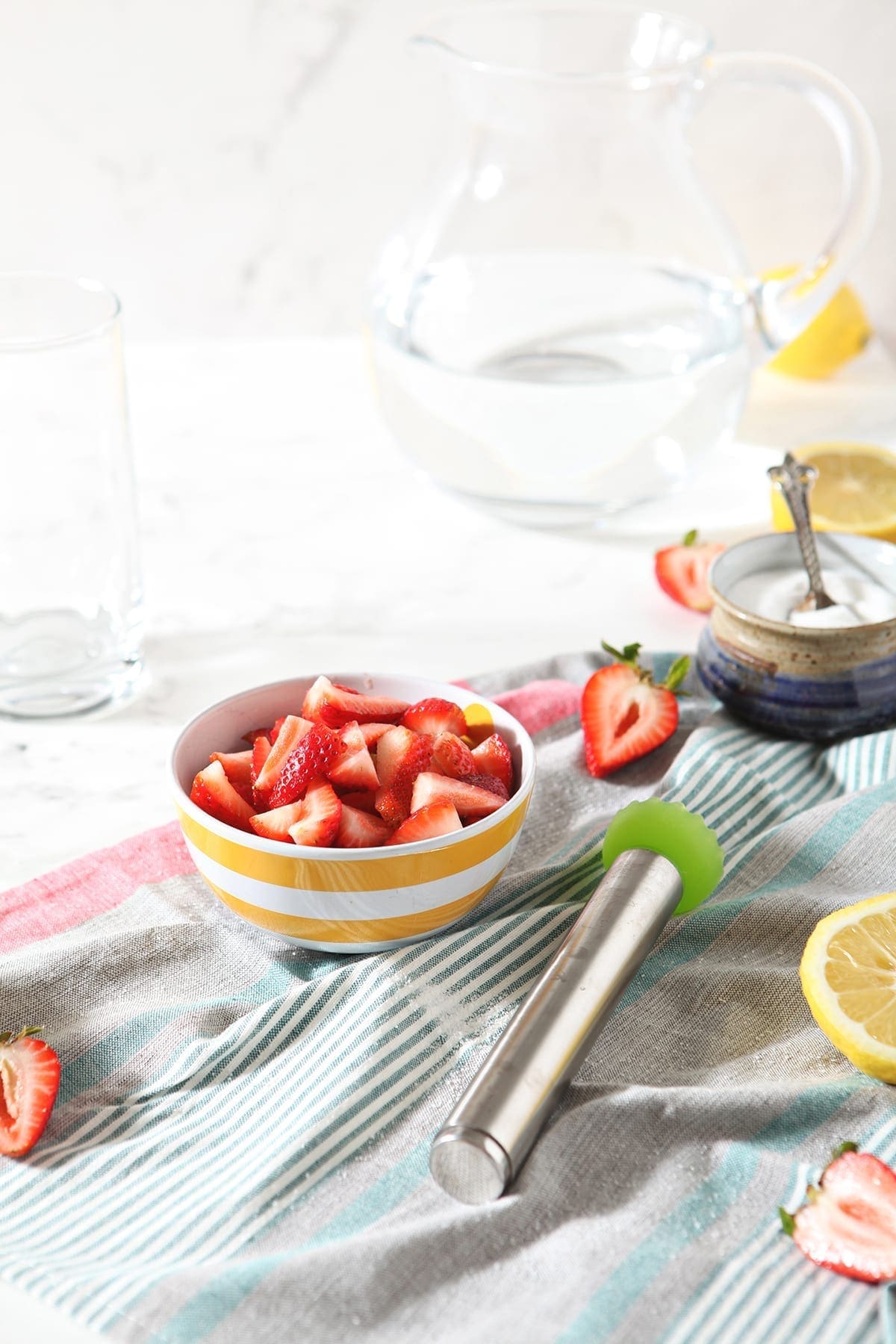 A bowl of strawberries, a pitcher of water and lemons are shown on marble