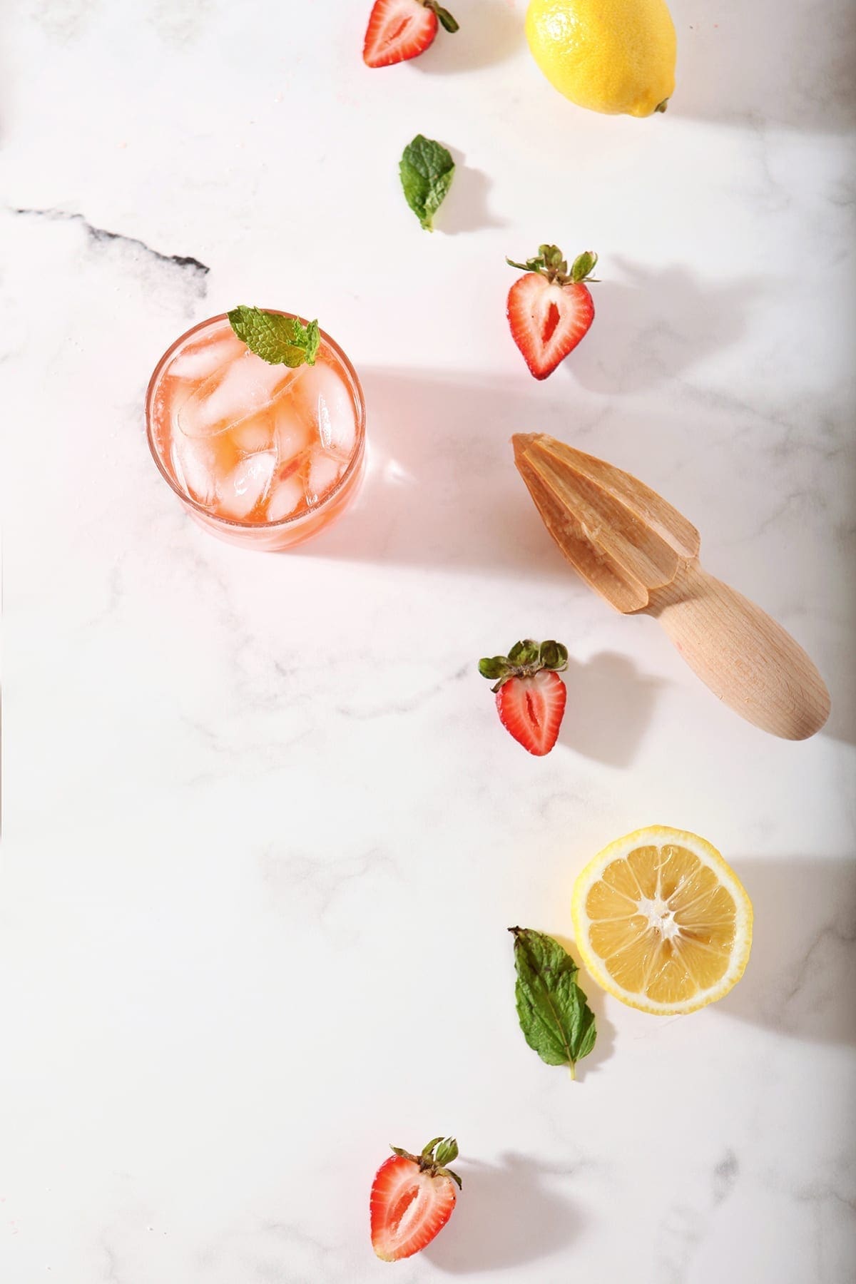 A glass of Strawberry Lemonade with its ingredients on a marble counter