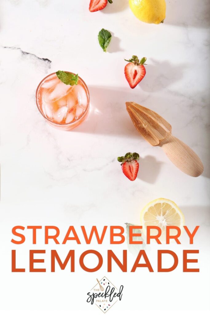 A glass of Strawberry Lemonade with its ingredients on a marble counter with text