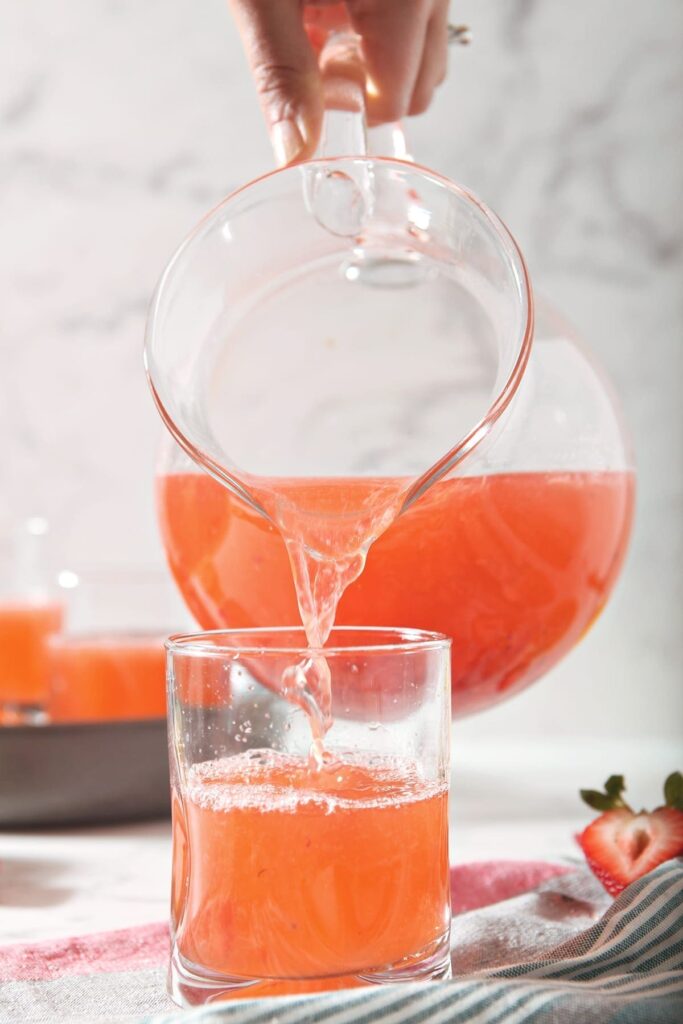 Strawberry Lemonade pours from a pitcher into a cup