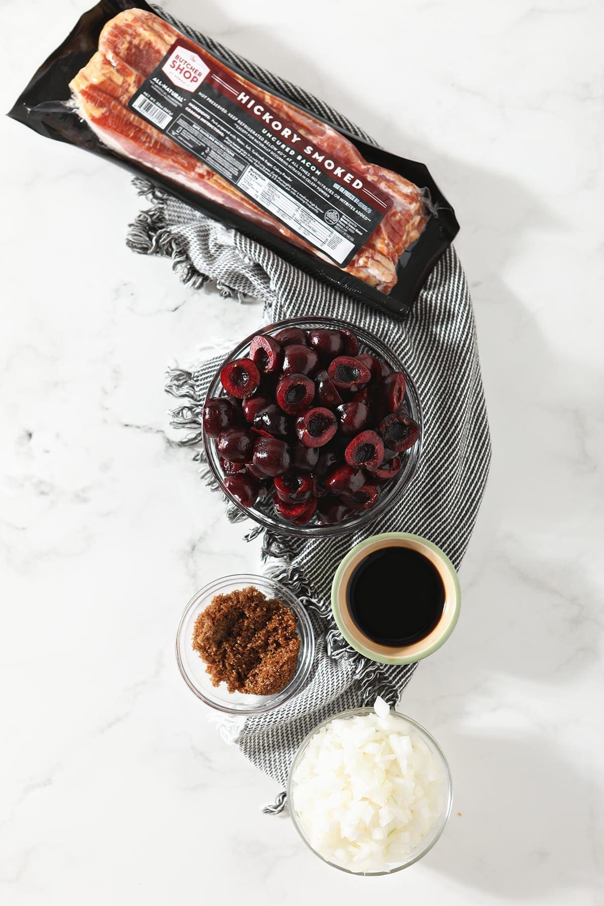 Products used to make Bacon Cherry Compote on a marble surface in bowls, from above