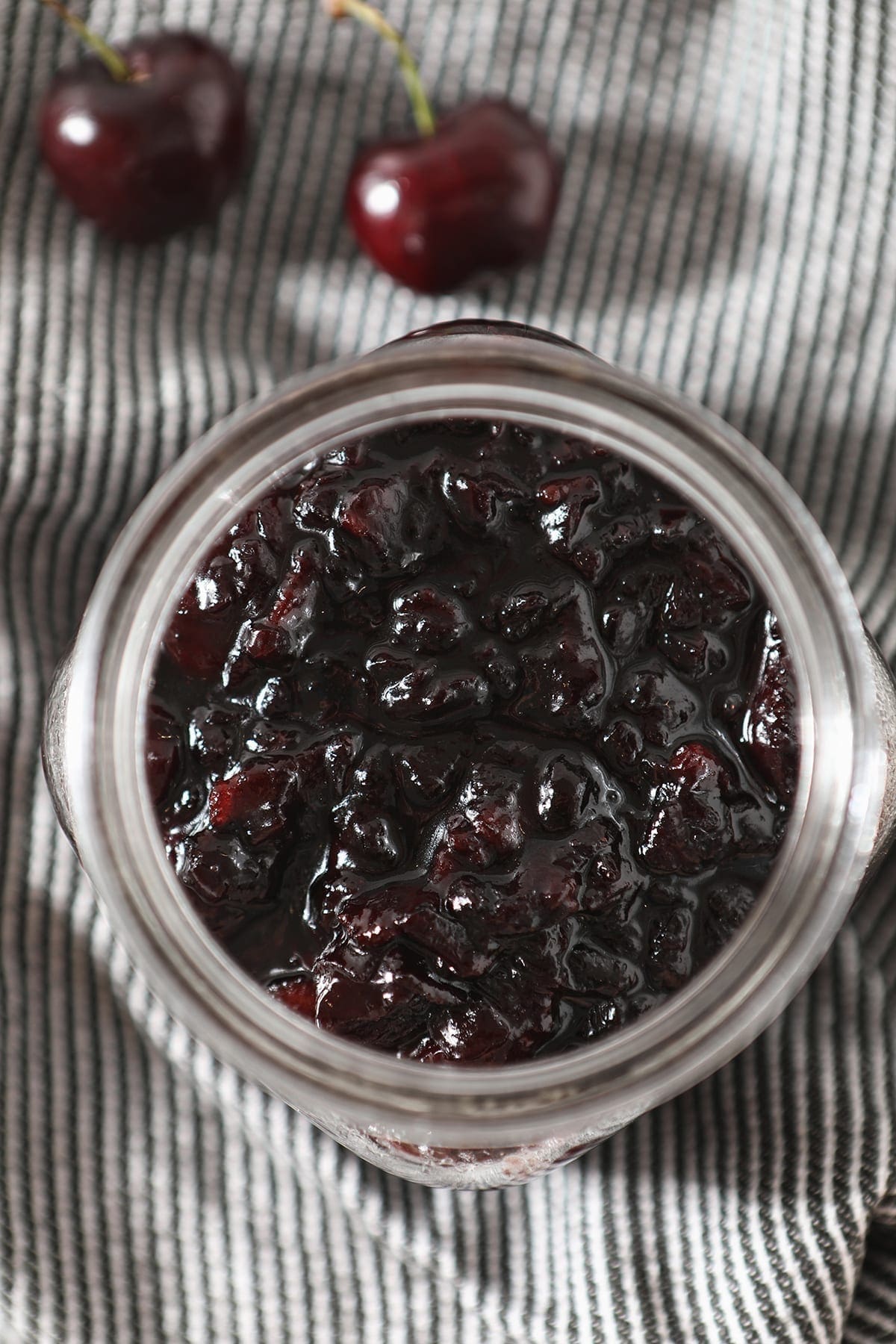 Close up looking into a jar of Bacon Cherry Compote from above on a grey and white striped towel