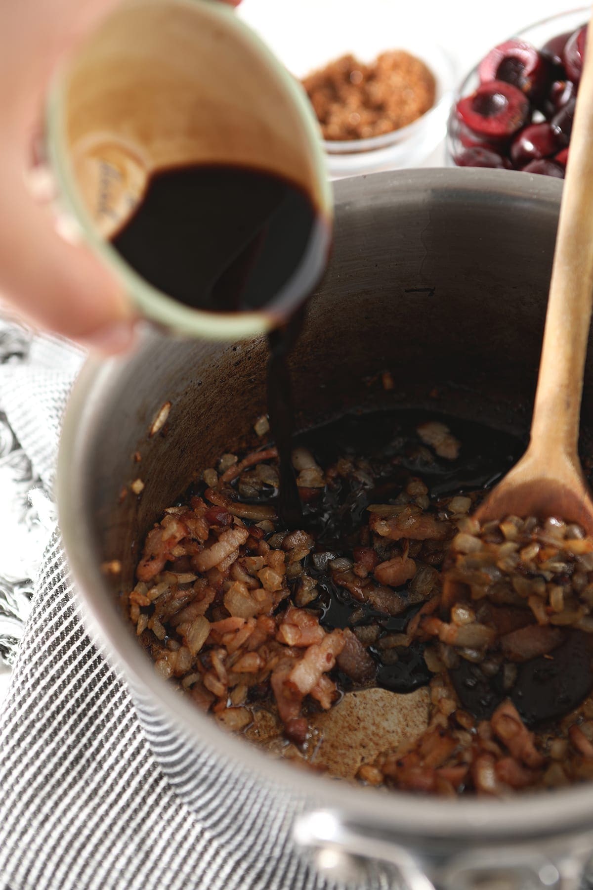 Balsamic vinegar is drizzled into a saucepan with cooked onion and bacon in it
