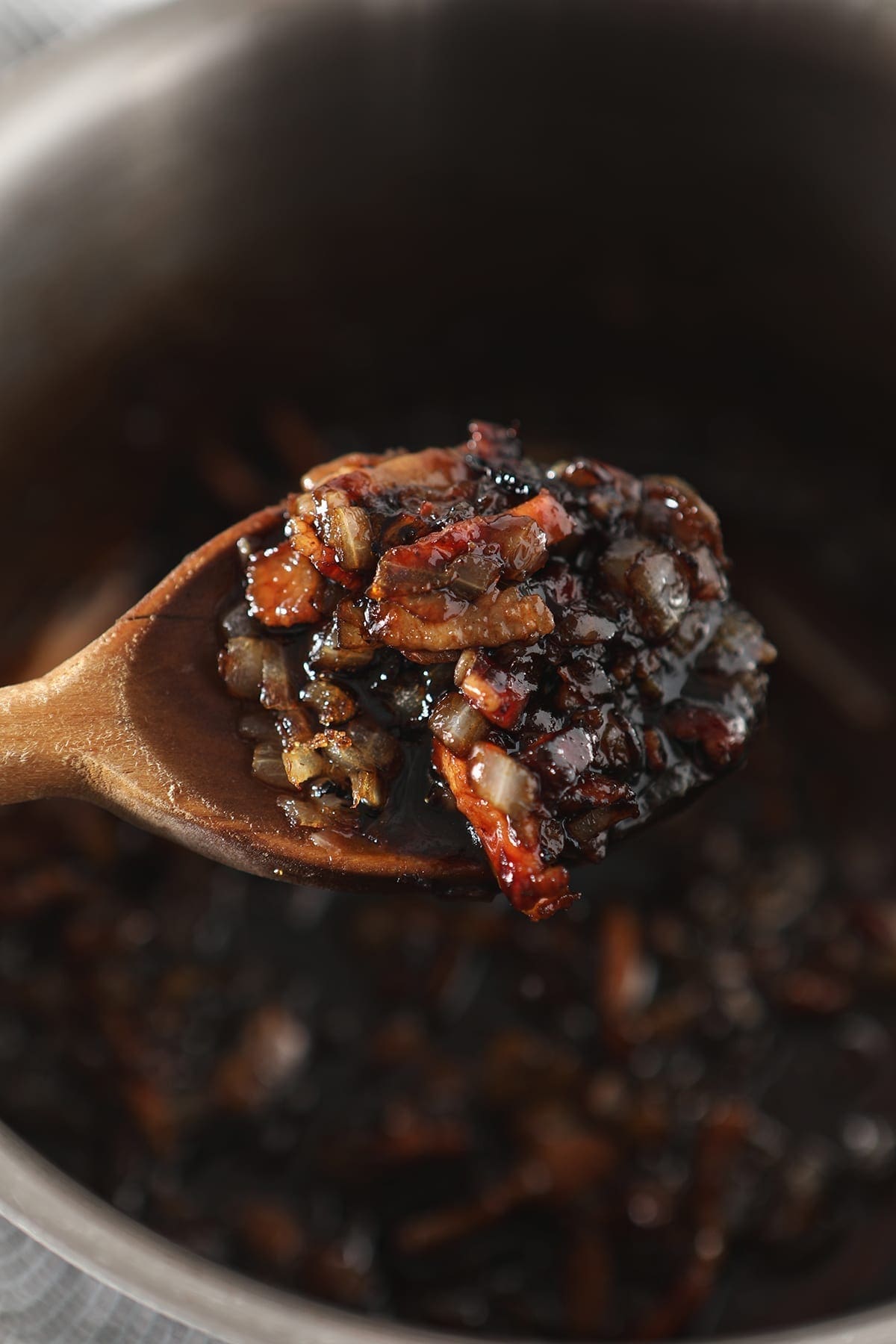 A wooden spoon holds components of Bacon Cherry Compote above a saucepan
