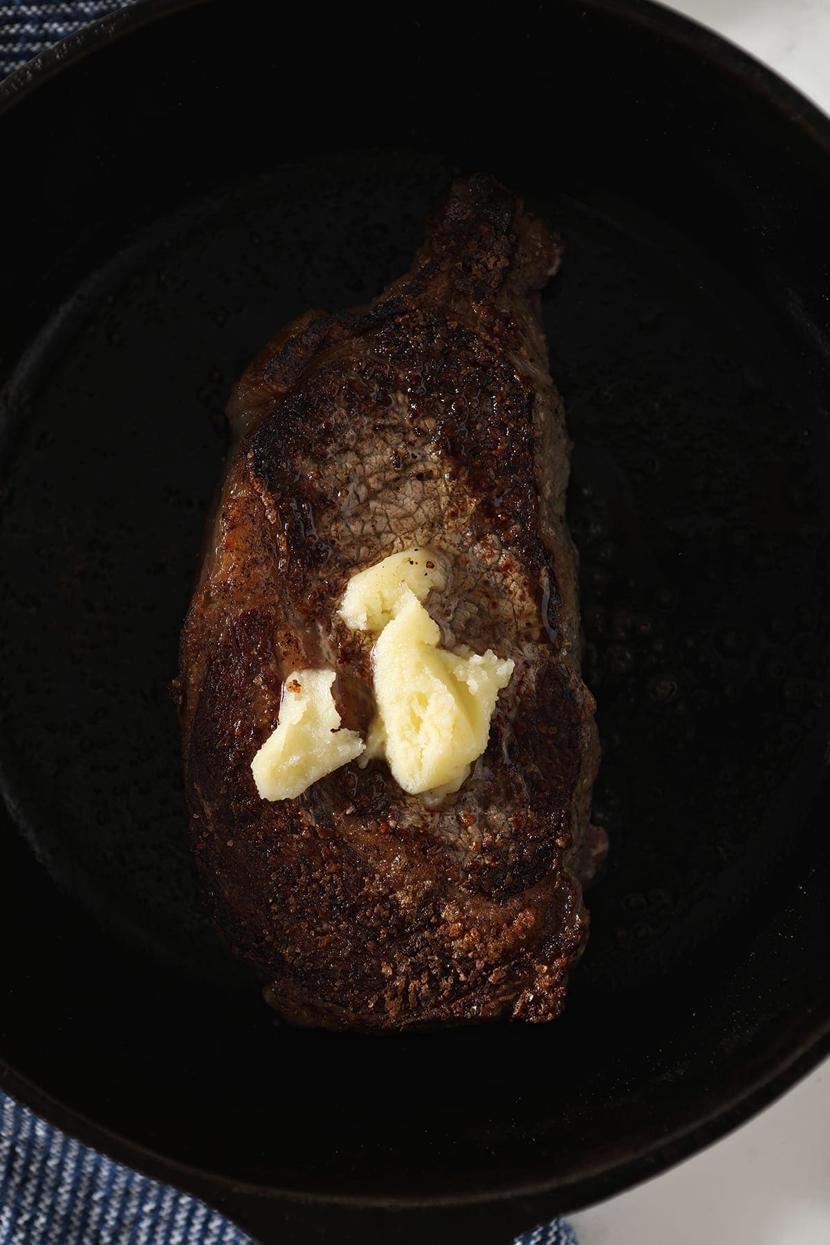 Ghee melts on top of a steak in a cast iron skillet as it cooks