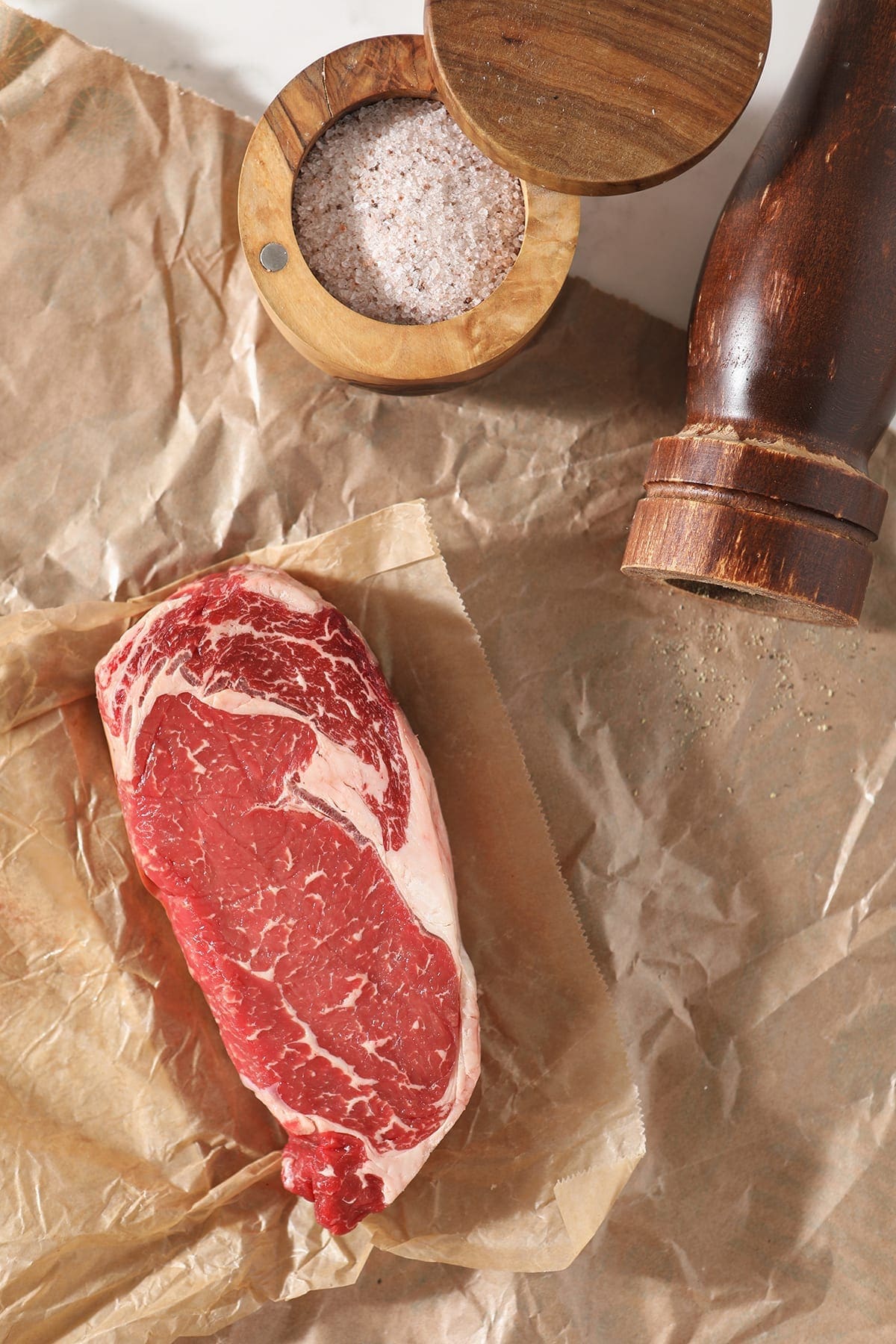 An uncooked ribeye steak on a piece of butcher paper with salt and pepper, from above