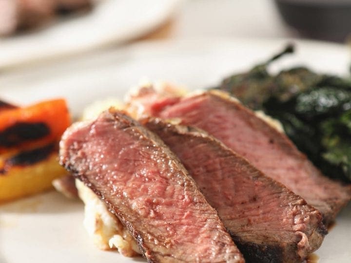 Close up of three slices of cast iron ribeye on a white plate with other sides