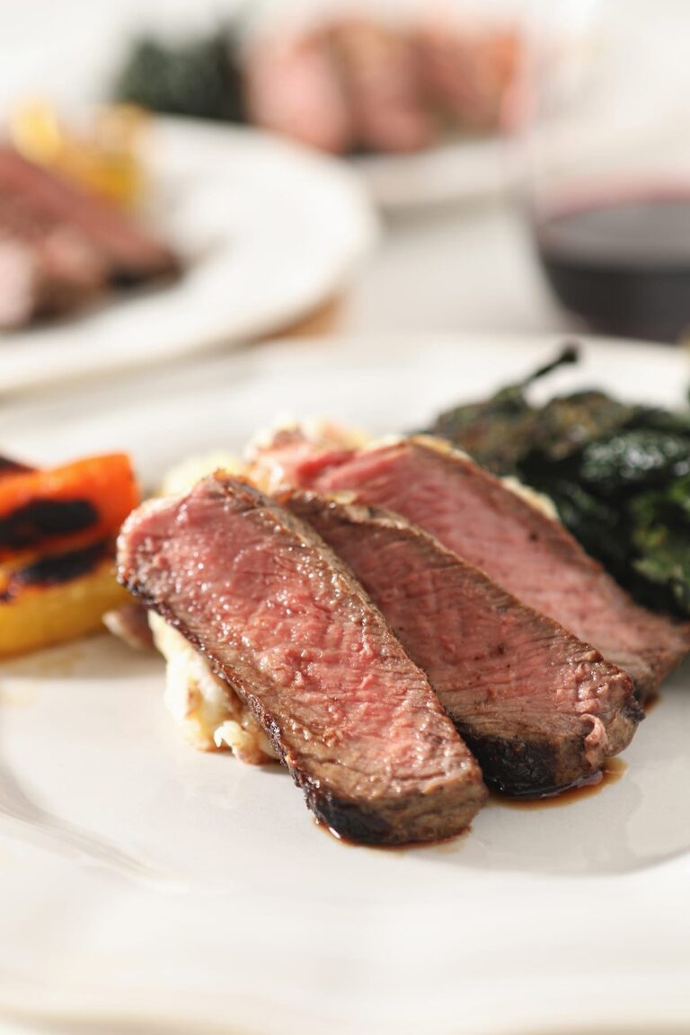 Close up of three slices of cast iron ribeye on a white plate with other sides