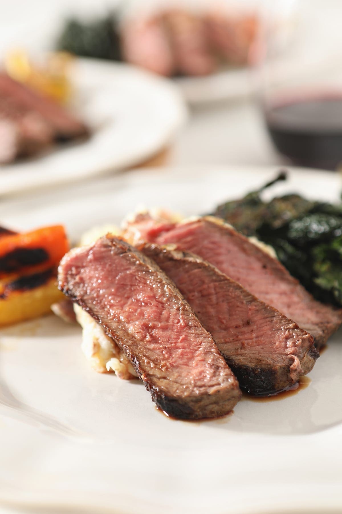 Close up of three slices of cast iron ribeye on a white plate with other sides