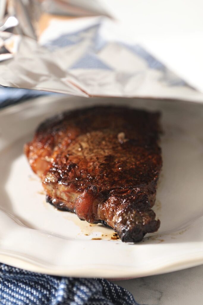 Aluminum foil is placed on top of a cooked ribeye steak before it rests