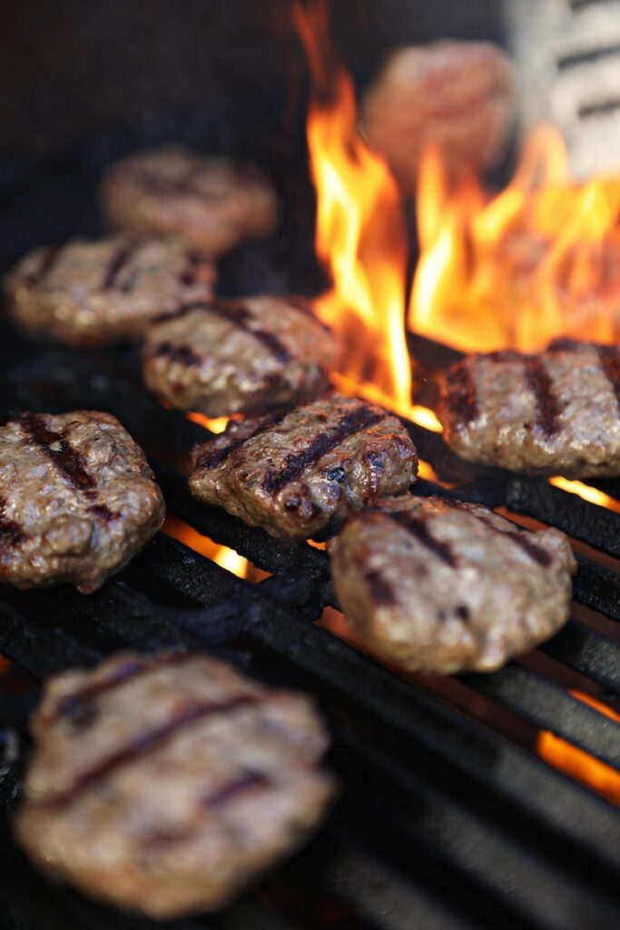 A spatula flips a beef slider on the grill as a flame flares up