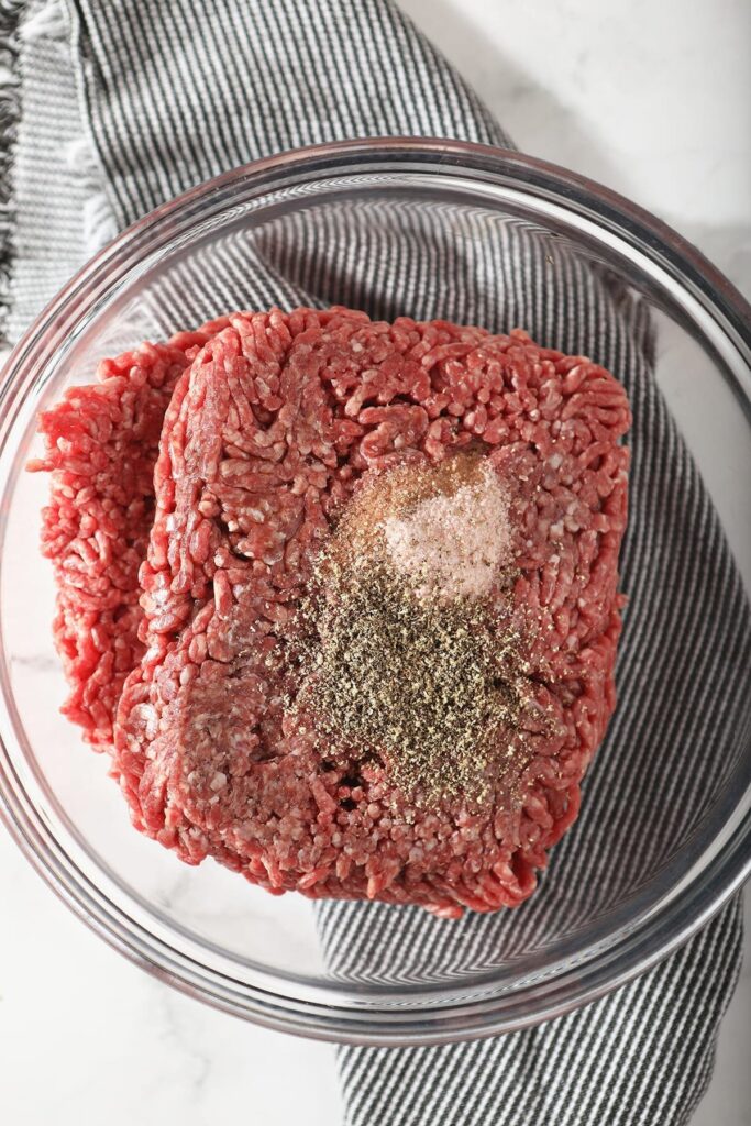 Ground beef with seasonings in a glass bowl on a grey striped towel