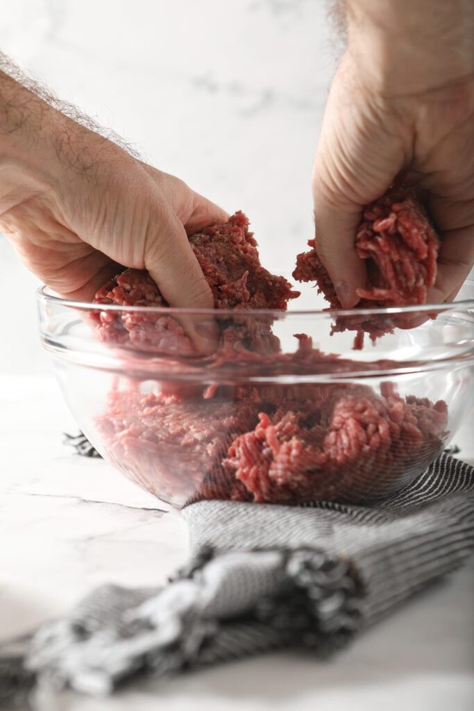 A man mixes ground beef with seasonings in a bowl with his hands