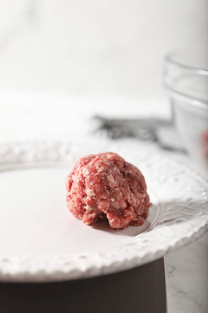 A ball of meat sits on a white plate on top of a kitchen scale before a slider is formed