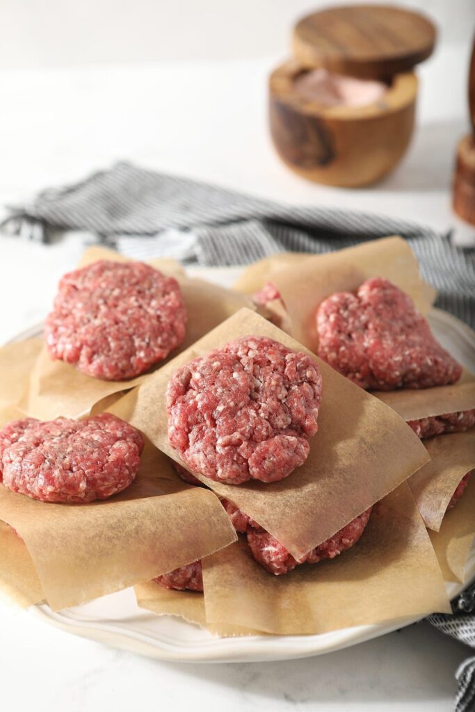 Slider patties stacked on top of each other sit on top of wax paper before grilling