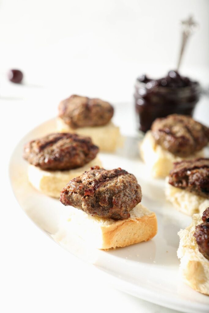 Hamburger slider patties sit on top of toasted buns before compote is added
