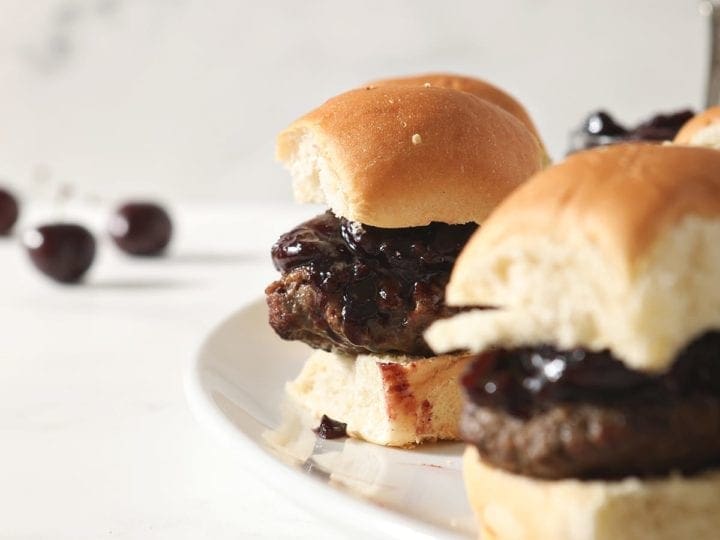 Hamburger sliders with Bacon Cherry Compote sit on a white platter before serving