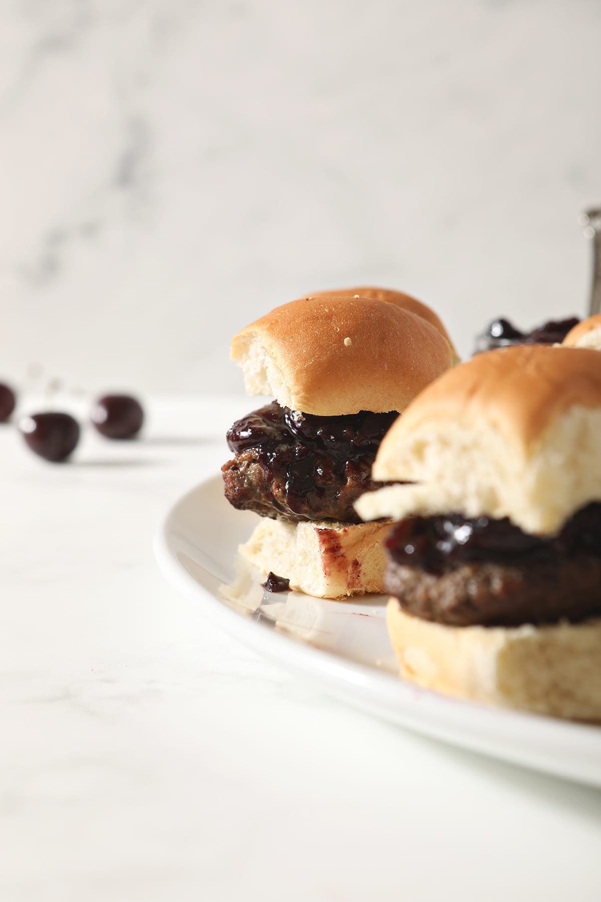 Hamburger sliders with Bacon Cherry Compote sit on a white platter before serving