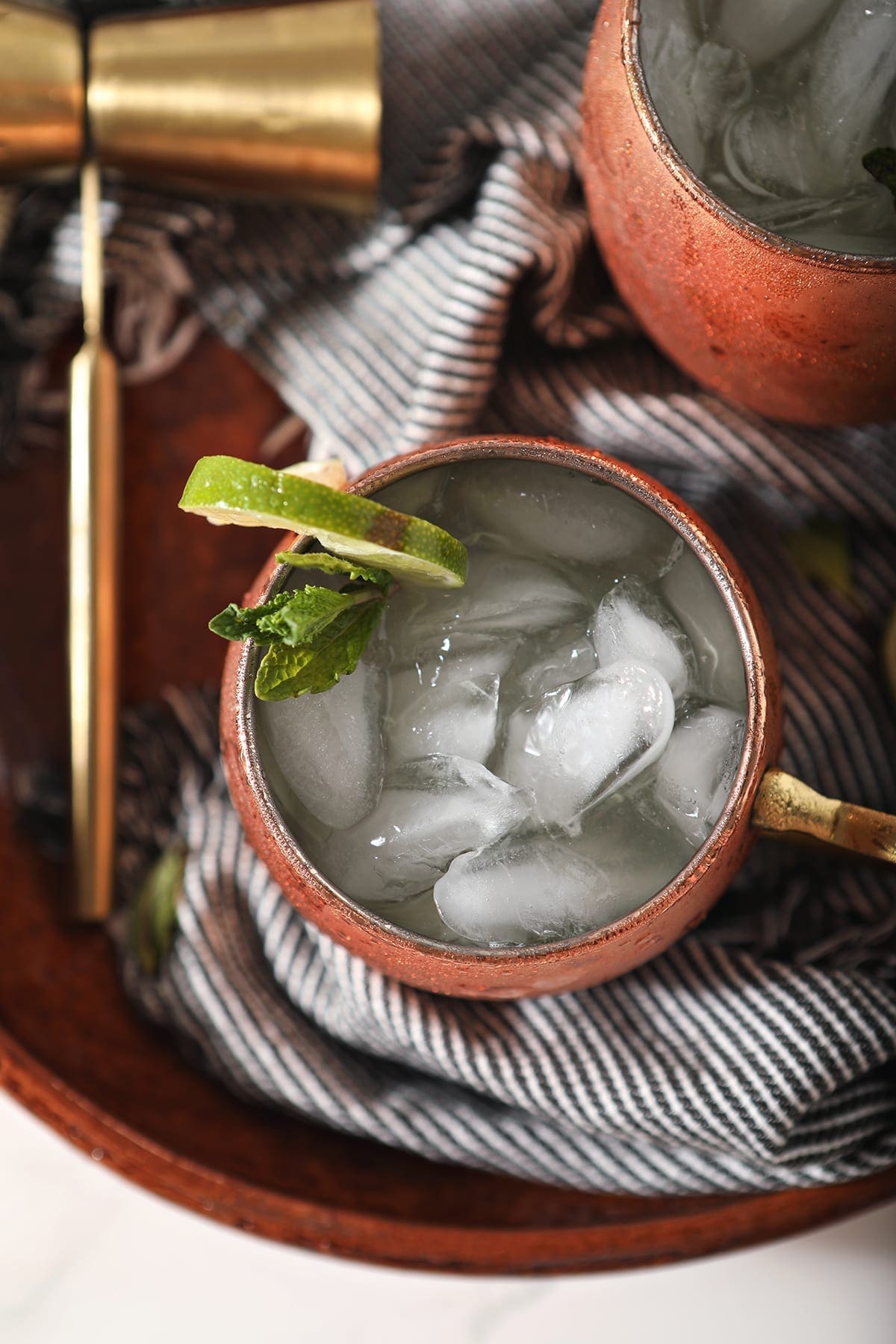 Overhead close up of a mule mug holding a Gin Gin Mule on top of a blue striped towel on a brown serving platter