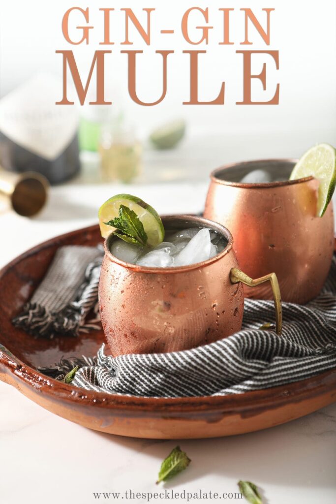 Two copper mugs ga rnished with lime rounds and mint are shown in a brown serving tray holding Gin Gin Mules, with text stating "Gin-Gin Mule"