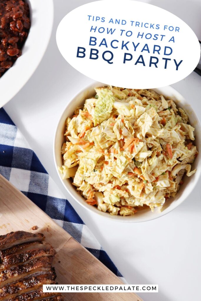 A bowl of honey mustard coleslaw near a blue buffalo check napkin, a brisket on a wooden cutting board and baked beans with the text "tips and tricks for how to host a backyard bbq party"